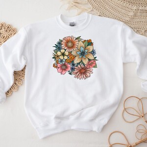 May include: White sweatshirt with a colorful floral print design. The flowers are pink, blue, yellow, and orange.