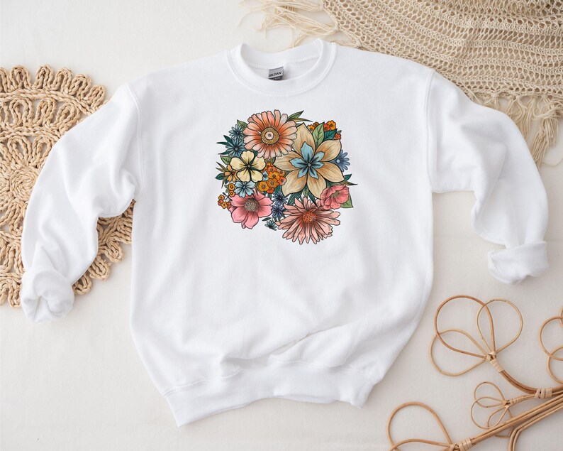 May include: White sweatshirt with a colorful floral print design. The flowers are pink, blue, yellow, and orange.