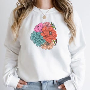 Pu&ograve; includere: Felpa bianca con stampa floreale colorata con fiori rosa, rossi, arancioni, blu e verdi.