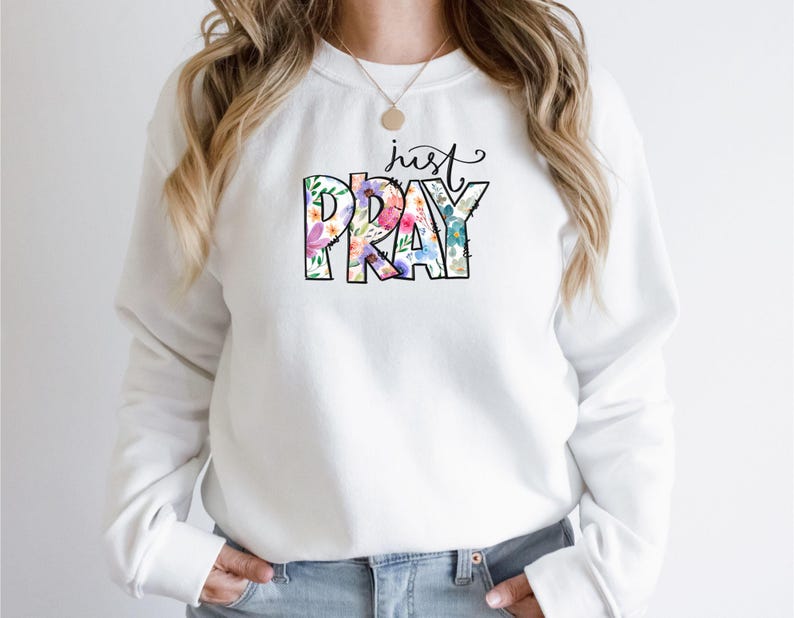 Pu&ograve; includere: Felpa bianca con un design floreale che dice "just pray" in testo nero.