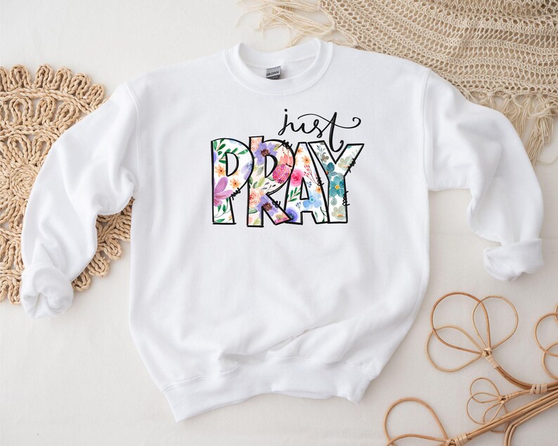 Pu&ograve; includere: Felpa bianca con il testo "just pray" in lettere nere con accenti floreali.