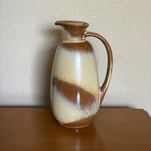 May include: A brown and white ceramic pitcher with a glaze finish. The pitcher has a rounded body and a handle.