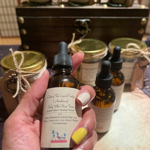 May include: A brown glass bottle with a dropper top and a label that reads "Chessy The Crystal Indigo Apothecary Ruby Who! Hair Tonic Growth Shine Healing Beauty 2oz www.chrissythecrystalindigo.com https://www.etsy.com/shop/Chrissy Crystalindigo".