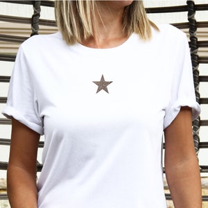 May include: A woman wearing a white t-shirt with a brown star on the front, sitting in a wicker chair.
