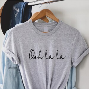 May include: Gray t-shirt with the text "Ooh la la" written in black cursive script.