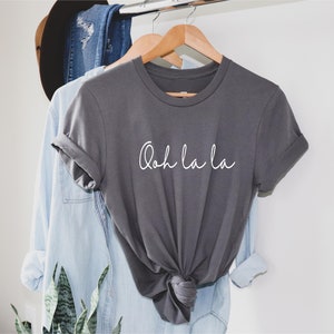 May include: A gray t-shirt with the text "Ooh la la" written in white cursive script.
