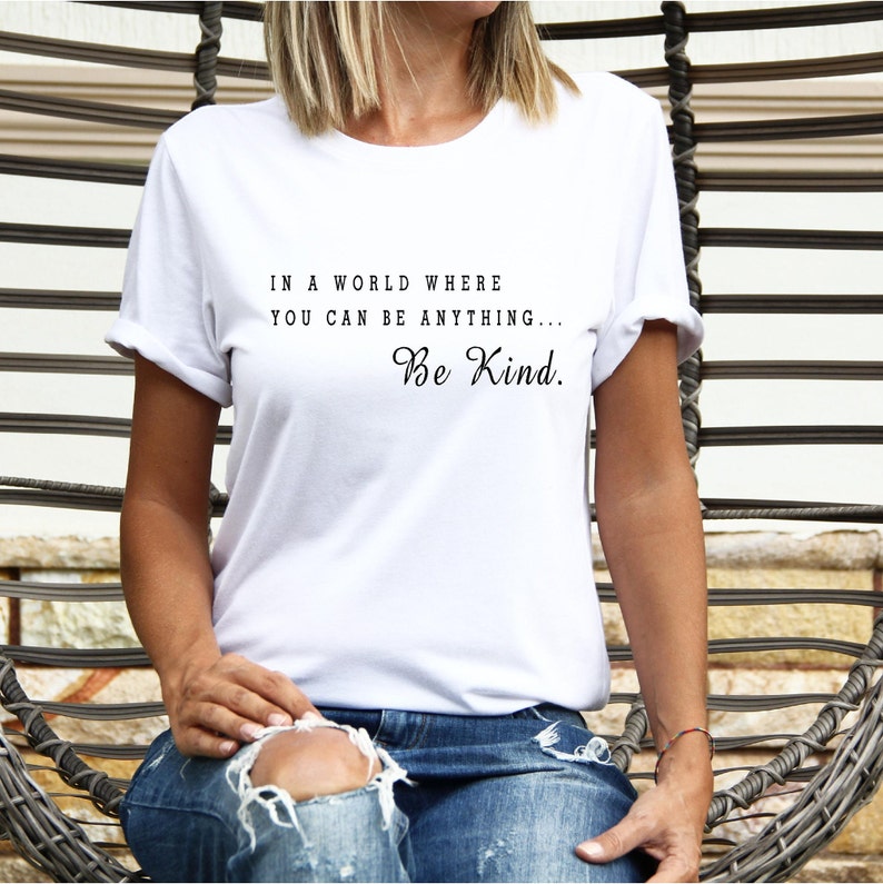 May include: White t-shirt with the text "In a world where you can be anything... Be Kind."