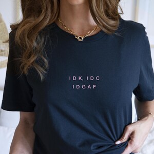 May include: A black t-shirt with the text "IDK, IDC IDGAF" printed in pink on the front.