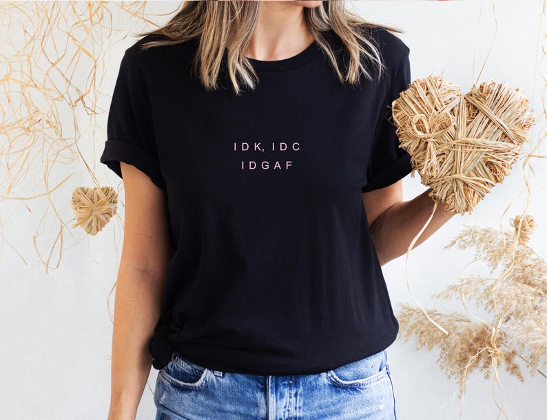 May include: A black t-shirt with the text "IDK, IDC IDGAF" printed in pink on the front.