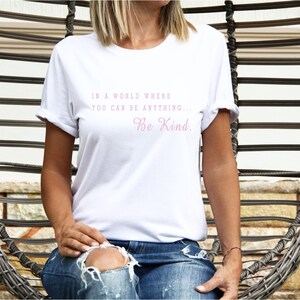 May include: White t-shirt with the text "In a world where you can be anything... Be Kind." printed in pink.