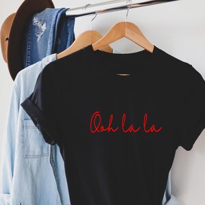 May include: Black t-shirt with red script that says "Ooh la la" hanging on a wooden hanger.