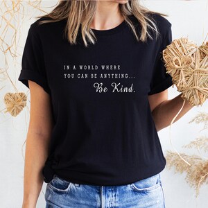 May include: Black t-shirt with white text that reads "In a world where you can be anything... Be Kind."
