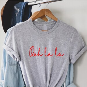 May include: Gray t-shirt with the phrase "Ooh la la" written in red cursive.