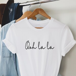 May include: White t-shirt with the text "Ooh la la" written in black cursive script.