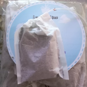 Pode incluir: Um close-up de um saquinho de chá branco com pó roxo claro dentro. O saquinho de chá está etiquetado como "Lemon Lime" e está embalado em um saco de plástico transparente.