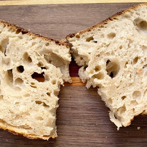 May include: Two halves of a loaf of bread, freshly cut, revealing a porous interior. The crust is a golden brown, contrasting with the lighter, airy crumb. The bread sits on a wooden cutting board.