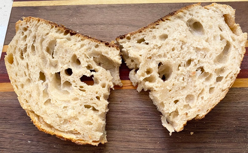 May include: Two halves of a loaf of bread, freshly cut, revealing a porous interior. The crust is a golden brown, contrasting with the lighter, airy crumb. The bread sits on a wooden cutting board.