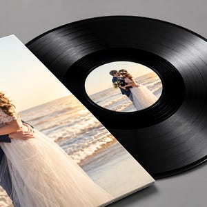 Puede incluir: Un disco de vinilo negro con una etiqueta central circular que muestra una fotografía de una pareja abrazándose en una playa al atardecer. El disco está parcialmente cubierto por una funda de álbum cuadrada con la misma foto de boda.
