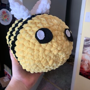Pode incluir: Uma abelha de pel&uacute;cia feita &agrave; m&atilde;o com corpo amarelo, listras pretas e asas brancas. A abelha tem olhos grandes e redondos com feltro preto e centros brancos. A pel&uacute;cia &eacute; macia e texturizada, perfeita para o quarto de uma crian&ccedil;a ou como item decorativo.