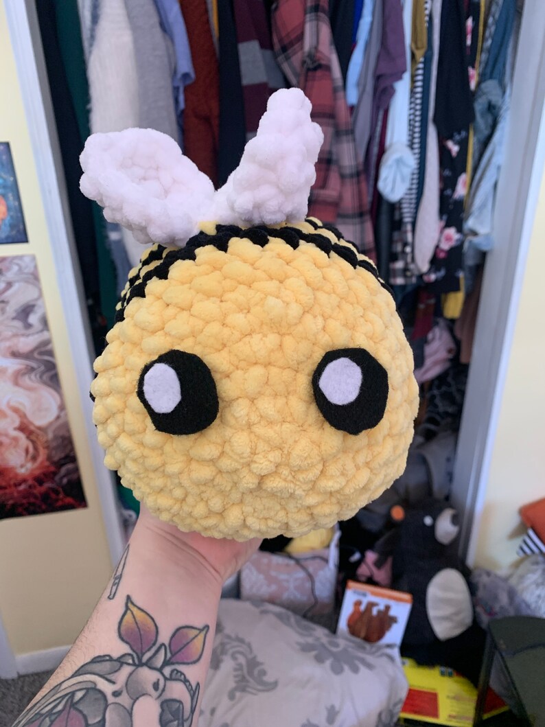 Pode incluir: Um brinquedo de abelha de pel&uacute;cia feito &agrave; m&atilde;o com corpo amarelo, listras pretas e asas brancas. A abelha tem olhos grandes e redondos com contornos pretos e centros brancos. O brinquedo &eacute; macio e redondo.