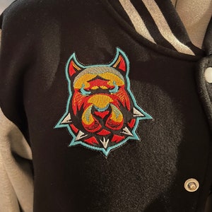May include: A black and gray varsity jacket with a red, yellow, and blue embroidered patch of a dog's face on the left side of the chest.