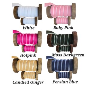 May include: Six sets of velvet ribbon spools in white, baby pink, hot pink, moss darkgreen, candied ginger, and persian blue. Each set includes one large and one small wooden spool wrapped with coloured velvet ribbon, labelled with the colour name.