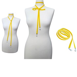 Pu&ograve; includere: Collana girocollo in velluto giallo con chiusura a fiocco e estremit&agrave; pendenti. La collana &egrave; esposta su un manichino, con una collana arrotolata separata. Le estremit&agrave; hanno piccoli accenti color argento.