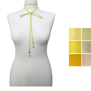 Pu&ograve; includere: Una collana girocollo giallo pallido con fiocco ed estremit&agrave; a nastro pendenti. Le estremit&agrave; del nastro hanno piccoli ciondoli rotondi color argento. A destra &egrave; mostrata una tavolozza di colori di tonalit&agrave; gialle.