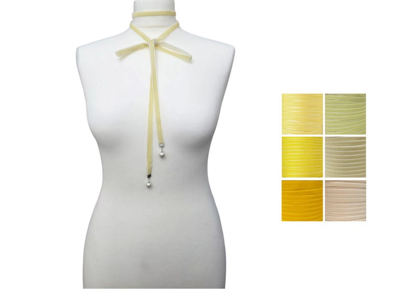 Pu&ograve; includere: Una collana girocollo giallo pallido con fiocco ed estremit&agrave; a nastro pendenti. Le estremit&agrave; del nastro hanno piccoli ciondoli rotondi color argento. A destra &egrave; mostrata una tavolozza di colori di tonalit&agrave; gialle.
