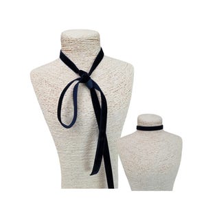 May include: A long, dark navy blue velvet ribbon necklace tied in a simple knot at the centre, displayed on a textured mannequin. Beside it, a second, shorter dark navy blue velvet choker sits snugly around the neck of a smaller mannequin.