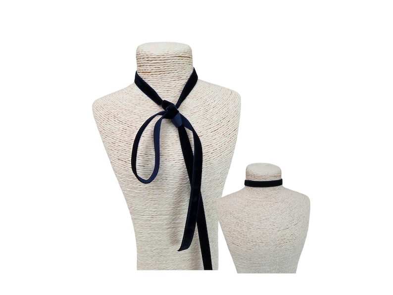 May include: A long, dark navy blue velvet ribbon necklace tied in a simple knot at the centre, displayed on a textured mannequin. Beside it, a second, shorter dark navy blue velvet choker sits snugly around the neck of a smaller mannequin.
