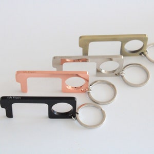 May include: Four keychains with a metal loop and a small metal hook. The keychains are in four different colours: black, copper, silver, and gold. The keychains have the text "Safe Fingers" engraved on them.