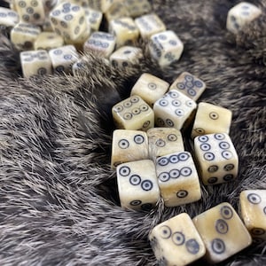 May include: A collection of bone dice with black dots on a brown fur background. The dice are arranged in a pile, with some of them partially obscured by others.