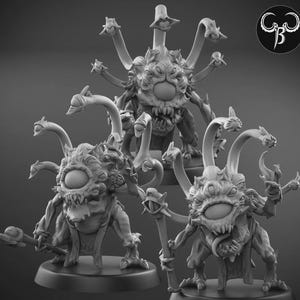 Puede incluir: Tres miniaturas de fantasía detalladas en escala de grises de un monstruo con un gran ojo central, múltiples tentáculos y una boca dentada. Las criaturas están posadas sobre bases redondas, una de ellas sosteniendo un bastón. Un logotipo está en la esquina superior derecha.