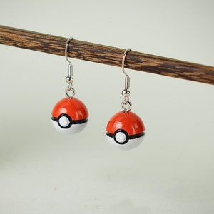 Könnte beinhalten: Ein Paar silberne Ohrringe mit roten und weißen Pokeball-Anhängern. Die Anhänger sind rund und haben einen schwarzen Umriss.