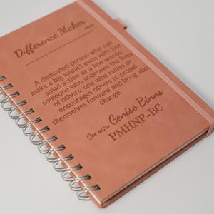 Puede incluir: Un cuaderno con espiral de color salmón. La portada presenta las palabras "Difference Maker" y una definición. También es visible el texto "See also: Genise Binns PMHNP-BC".