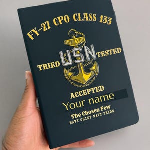 Könnte beinhalten: Ein dunkelblaues Notizbuch mit einer goldenen Ankergrafik und dem Text FY-27 CPO CLASS 133, TRIED USN TESTED, ACCEPTED, Your name, The Chosen Few und NAVY CHIEF NAVY PRIDE in goldener und weißer Schrift auf dem vorderen Einband.