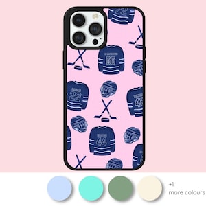 May include: A phone case with a light pink background featuring a repeating pattern of dark blue ice hockey jerseys with numbers, hockey helmets, crossed hockey sticks, and pucks. The case has a black border and a cutout for the camera lens.