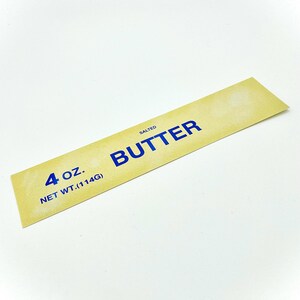 May include: A yellow rectangular label with blue text that reads "SALTED BUTTER" and "4 oz. NET WT. (114G)".