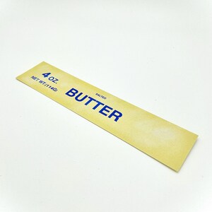 May include: A yellow label with blue text that reads "4 oz. NET WT. (114G) SALTED BUTTER".