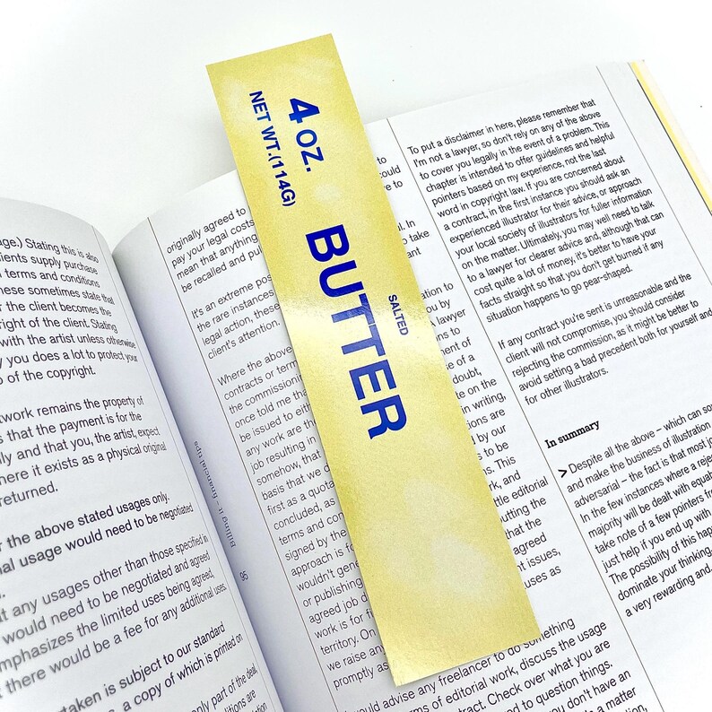 May include: A yellow bookmark with the words "SALTED BUTTER" in blue lettering and "4 oz. NET WT.(114G)" in black lettering. The bookmark is made of a glossy material and has a gold sheen.