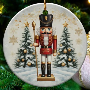 May include: A circular Christmas decoration depicting a nutcracker soldier in a red and black uniform, holding a staff. The background shows two Christmas trees and snowflakes. The ornament is suspended on a Christmas tree.