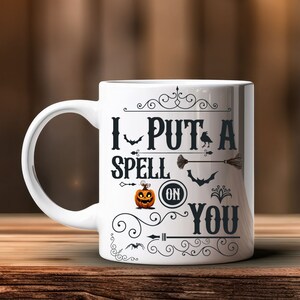 May include: White ceramic mug with a black and white design that says "I Put A Spell On You". The design includes a pumpkin, bats, a broom, and an arrow.