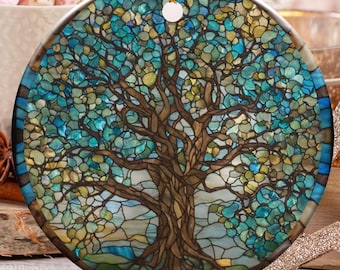 May include: A round Christmas ornament with a stained-glass tree design. The ornament is blue, green, and brown, with a gold string for hanging. The background includes candy canes, a mug of marshmallows, and other holiday decorations.