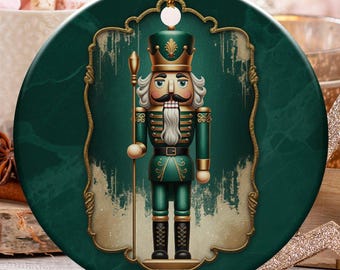 Könnte beinhalten: Runder Weihnachtsschmuck mit einem grün-goldenen Nussknacker-Design. Der Schmuck wird an einem goldenen Faden aufgehängt. Der Hintergrund umfasst Marshmallows, Zuckerstangen und andere Weihnachtsdekorationen.