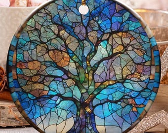 May include: A round Christmas ornament with a stained-glass tree design in shades of blue, green, and gold. The ornament hangs from a gold string. The background includes a cup of marshmallows, candy canes, and other holiday decorations.