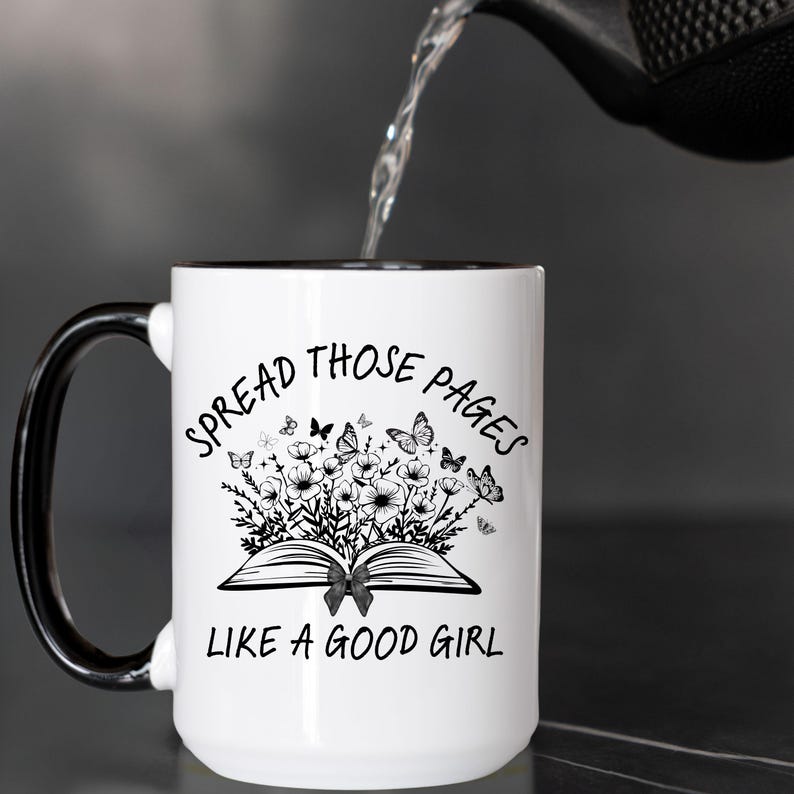 Puede incluir: Taza de cer&aacute;mica blanca con asa y borde negros. La taza presenta el texto "SPREAD THOSE PAGES LIKE A GOOD GIRL" alrededor de un dise&ntilde;o floral y de mariposas. Se est&aacute; vertiendo agua en la taza.