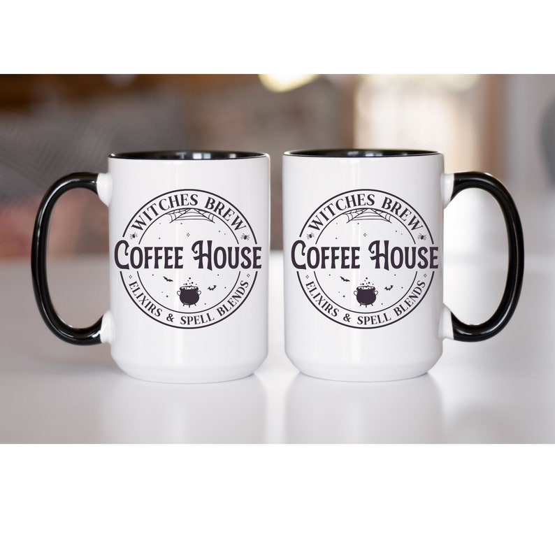May include: Two white coffee mugs with black rims. The mugs have a black and white graphic of a cauldron with bats and the text "Witches Brew Coffee House Elixirs & Spell Blends".