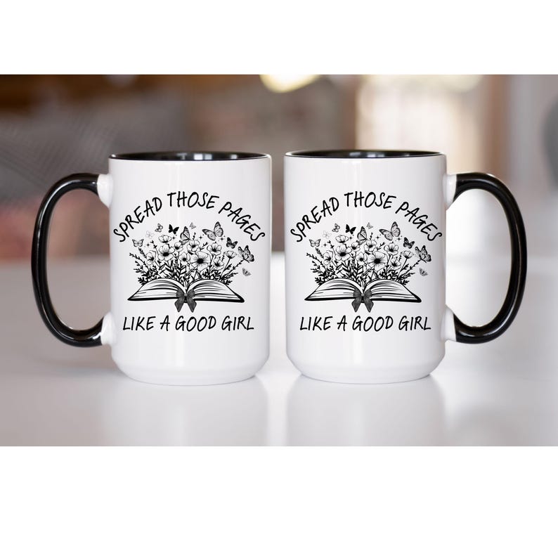 Puede incluir: Dos tazas blancas con asas y bordes negros. Cada taza presenta el texto "SPREAD THOSE PAGES LIKE A GOOD GIRL" con un dise&ntilde;o floral y de mariposas sobre un libro abierto.