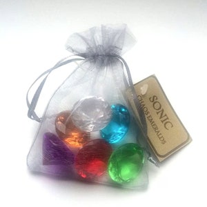 May include: A set of seven colourful, clear plastic gems in a grey organza bag with a brown tag that reads "SONIC CHAOS EMERALDS".